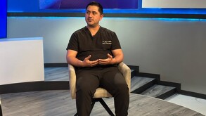 Se observa a un hombre que viste un uniforme de Doctor, está sentado y hablando.