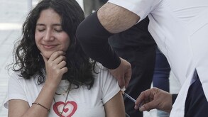 Mujer sonríe y se lleva la mano al rostro mientras es vacunada por una enfermera.