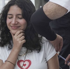 Mujer sonríe y se lleva la mano al rostro mientras es vacunada por una enfermera.