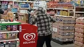Mujer vista de espaldas con un abrigo a cuadros y las manos levantadas adentro de un Bodega Aurrera con empleados frente a ella