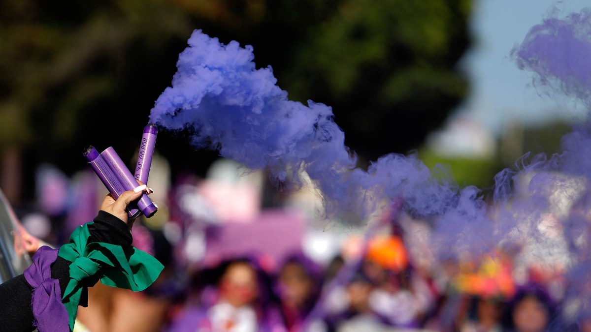 Brazo de una mujer durante una marcha del 8M con una bengala de humo morado en la mano.