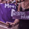 Mujer vista del cuello hacia abajo con un cartel morado con la leyenda 