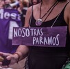 Mujer vista del cuello hacia abajo con un cartel morado con la leyenda 