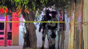 Dos elementos de la Guardia Nacional sujetando armas largas mientras resguardan el exterior de una casa acordonada por cinta policiaca