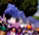 Brazo de una mujer durante una marcha del 8M con una bengala de humo morado en la mano.