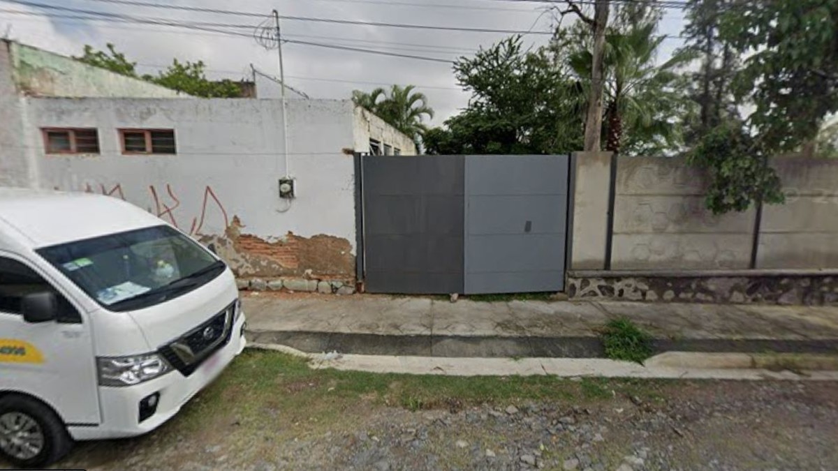 Vista del exterior de un predio en Zapopan con un portón gris y muros de concreto. Una vagoneta blanca estacionada enfrente.