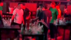Hombres dentro de una discoteca de Perú con luz tenue roja parados alrededor de mesas con botellas de cristal vacías
