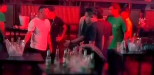 Hombres dentro de una discoteca de Perú con luz tenue roja parados alrededor de mesas con botellas de cristal vacías