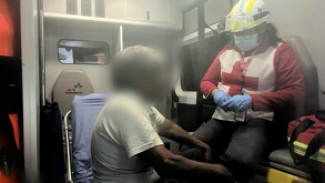 Se observa a un hombre de canas y con rostro con blur, sentado en una ambulancia, siendo atendido.