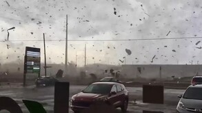 Tornado pasando por un estacionamiento de EU con escombro y objetos volando por los aires con automóviles estacionados en el sitio