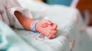 Mano de un recién nacido con una cinta azul en la muñeca recostado sobre una cama de hospital