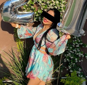 Se observa a una joven con unos globos en la mano, está sonriendo y viste un vestido.