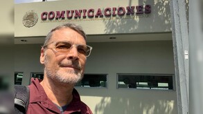 Erik Saracho Aguilar delante de las oficinas de la SICT vistiendo una playera tipo polo color roja y una mochila al hombro