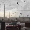 Tornado pasando por un estacionamiento de EU con escombro y objetos volando por los aires con automóviles estacionados en el sitio