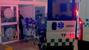 Paramédicos de la Cruz Verde ingresando a un hospital a un joven acostado en una camilla y cubriéndose con un abrigo azul tras salir de una ambulancia