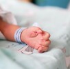 Mano de un recién nacido con una cinta azul en la muñeca recostado sobre una cama de hospital