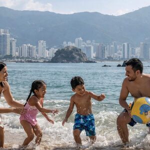 Familia disfrutando de las vacaciones de semana santa y jugando frente al mar de Acapulco con una pelota en un día soleado.