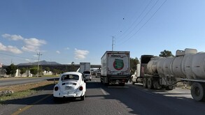 Se observa varios autos parados sobre una carretera; hay tráileres.