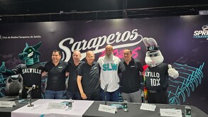 Se observa a varios hombres parados, tienen una mesa enfrente.