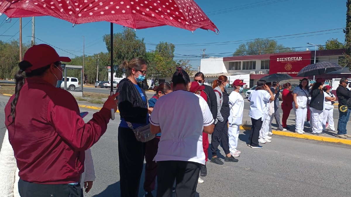 Se observa a hombres y mujeres en fila, hay un señor que trae en las manos un paraguas color guindo.