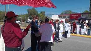 Se observa a hombres y mujeres en fila, hay un señor que trae en las manos un paraguas color guindo.