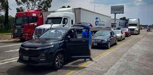 un hombre al aldo de su auto y otros vehículos varados en un bloqueo en la autopista méxico puebla