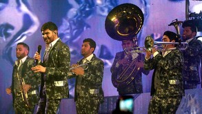 Cantantes y músicos de la Banda El Recodo en el escenario durante un concierto tocando varios instrumentos