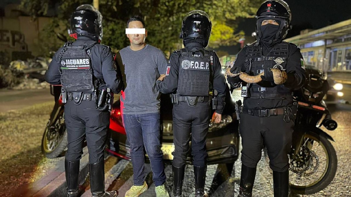 Joven con los ojos censurados  por un recuadro blanco siendo detenido por los brazos por policías de Guadalajara con motos detrás