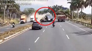 Camión de carga impactándose contra otros vehículos en el carril contrario en medio de una carretera y una nube de humo