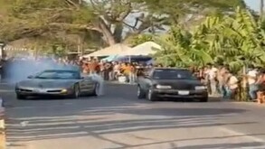 Un automóvil negro y otro gris con humo saliendo de su parte exterior con varias personas a los costados observando un evento de arrancones en Michoacán