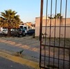 Vista exterior del fraccionamiento Los Agaves con un portón negro abierto y al interior un camión de transporte de personal con dos autos estacionados al ladod