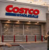 Clientes esperan frente a la entrada cerrada de una tienda Costco con un carrito de compras.