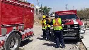 Se observa a tres personas con unifromes en tonos amarillos y rojos, y un camión de bomberos rojo.