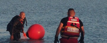 Dos elementos de Protección Civil Jalisco con una boya y chaleco de rescate dentro del agua en la presa La Reventada de Tlajomulco