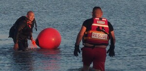 Dos elementos de Protección Civil Jalisco con una boya y chaleco de rescate dentro del agua en la presa La Reventada de Tlajomulco