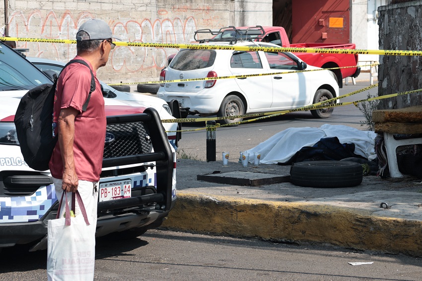 Hombre mira el cuerpo sin vida de una persona que ha sido tapado con una cobija y rodeado de veladoras.