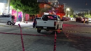 Camioneta Ford color blanco en medio de la calle dentro de un área acordonada por cintas policiacas con personas, patrullas y policías al frente