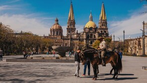 Elementos de la Policía Montada sobre caballos delante de una fuente con personas alrededor y la Catedral de Guadalajara en el fondo durante un día soleado