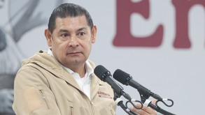 Hombre vestido con sudadera hace una expresión seria frente al micrófono.