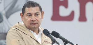 Hombre vestido con sudadera hace una expresión seria frente al micrófono.