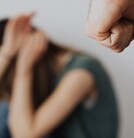 Puño de hombre amenazando a mujer que se cubre el rostro