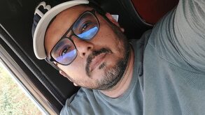 Hombre con lentes y gorra posa para una fotografía desde un vehículo.