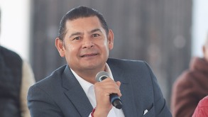 Hombre vestido de traje sonriendo mientras toma un micrófono con la mano.