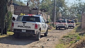 Tres patrullas de la Policía Municipal de Tlaquepaque estacionadas sobre un camino de tierra con cintas policiacas acordonando el área con viviendas alrededor