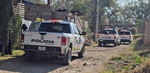 Tres patrullas de la Policía Municipal de Tlaquepaque estacionadas sobre un camino de tierra con cintas policiacas acordonando el área con viviendas alrededor