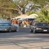 Un automóvil negro y otro gris con humo saliendo de su parte exterior con varias personas a los costados observando un evento de arrancones en Michoacán