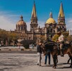 Elementos de la Policía Montada sobre caballos delante de una fuente con personas alrededor y la Catedral de Guadalajara en el fondo durante un día soleado