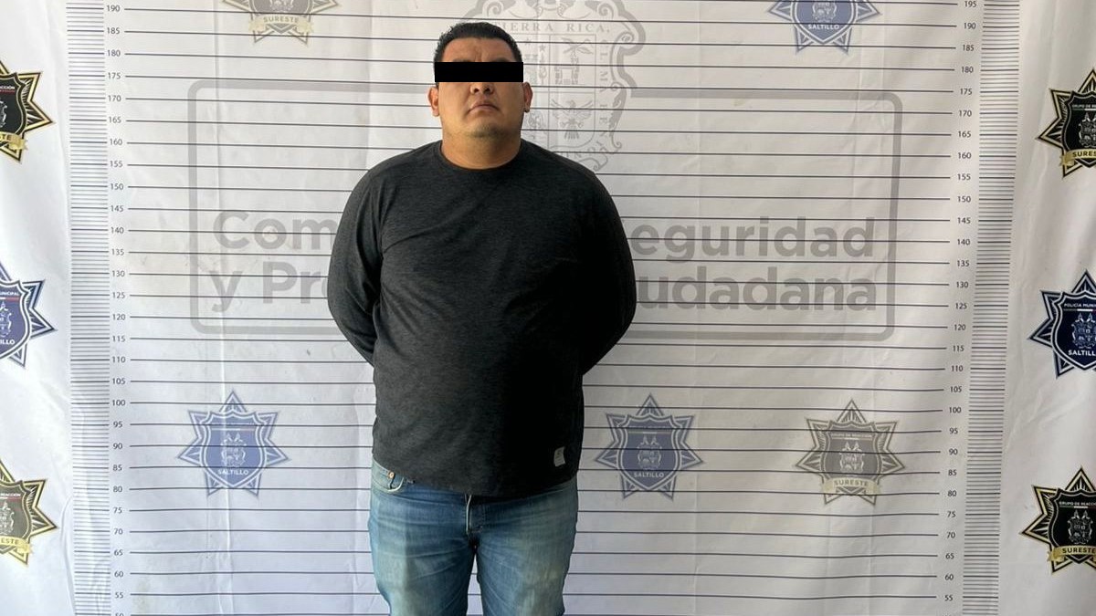 Se observa a un hombre parado, con ojos cubiertos; viste pantalón de mezclilla y playera negra.