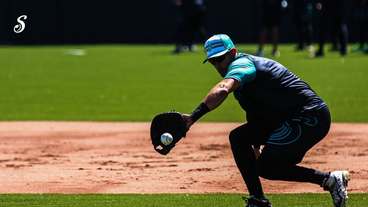Un jugador de los Saraperos de Saltillo se agacha para atrapar la pelota durante una jugada defensiva en el infield, sobre el campo de tierra y césped.