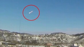 Captura de pantalla del video de un meteorito resaltado con un círculo rojo cruzando el cielo mientras cae en una zona montañosa con árboles en Ohio